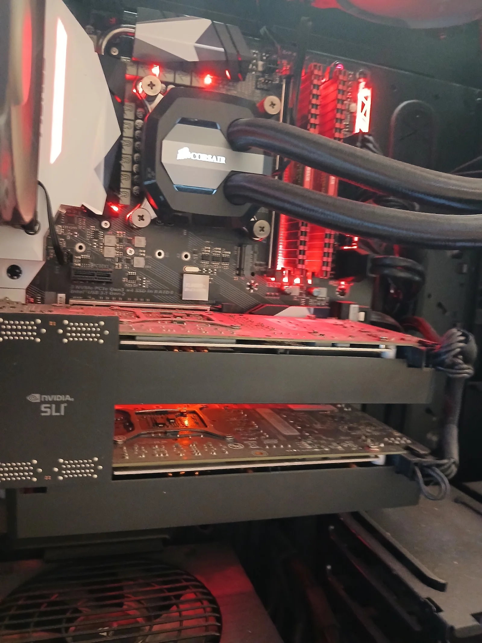 Dual NVIDIA graphics cards bridged in SLI inside a custom red-themed gaming PC with Corsair AIO water cooler and red-lit Corsair Vengeance RAM, on the bench in Harold Hill Romford